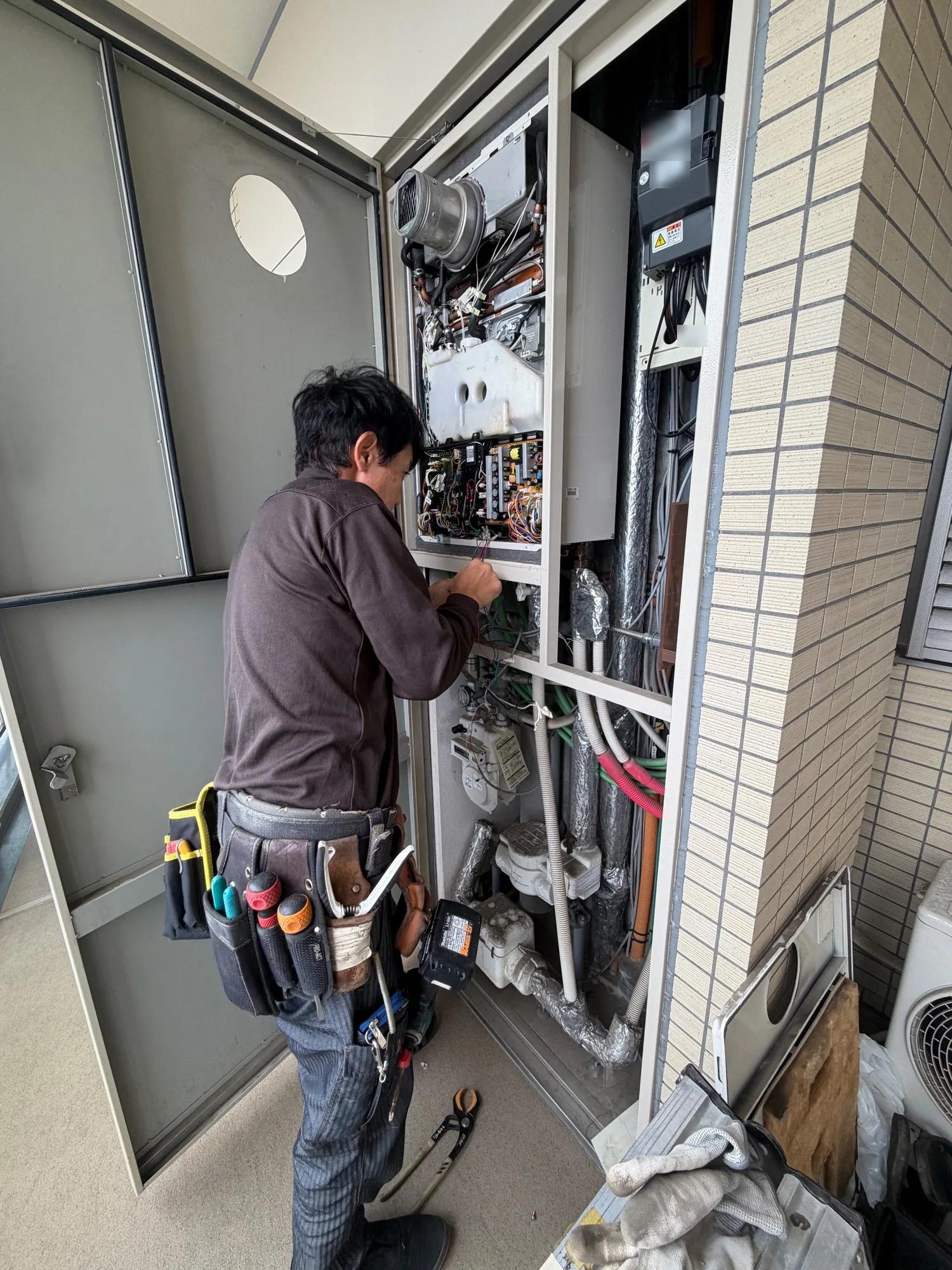 PS扉の中に設置されていた既設の給湯器。前面カバーを外した状態で、内部の基板・配線と下部に束ねられた配管がつながっている。右隣は電気の引き込み区画で、機器を納められる幅と奥行きが決まっている