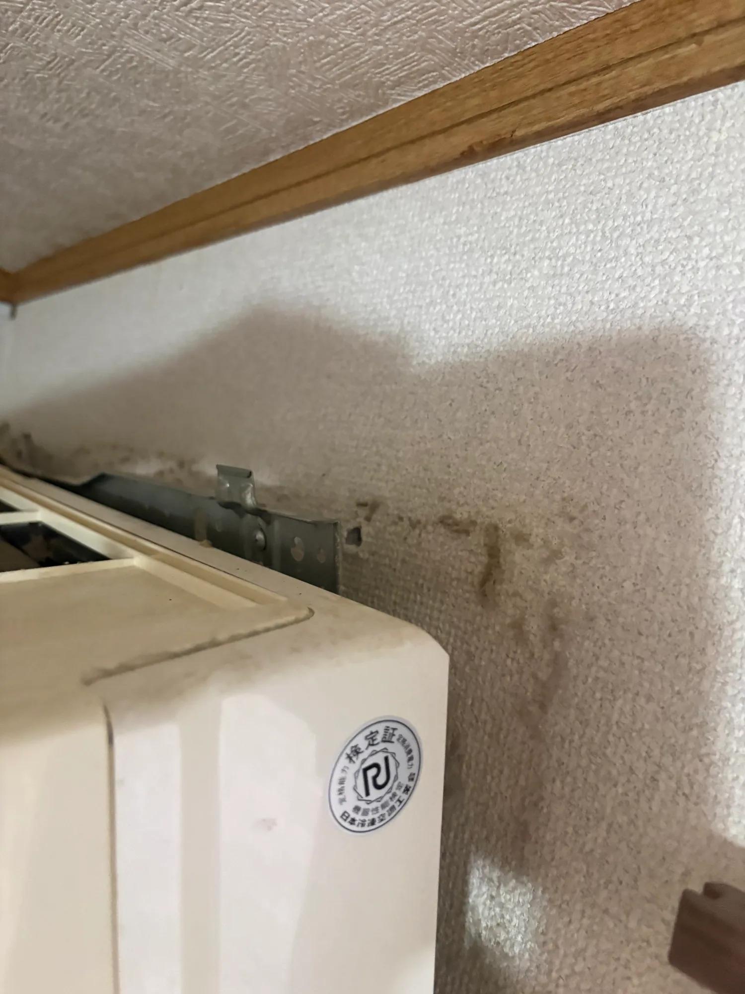 施工前の室内機。上部が壁から浮いて前へ傾いている。上部2箇所のビスは石膏ボードに刺さっているだけで、下地（垂木）にもボードアンカーにも掛かっていなかった