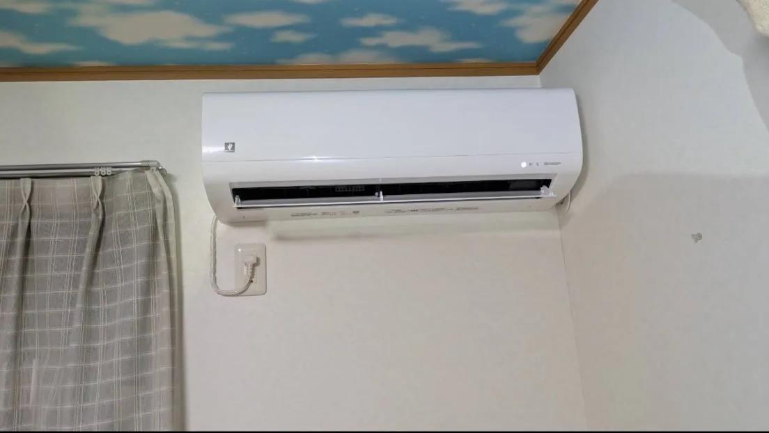 カーテンレールの上の壁に取り付けた室内機。天井との間が狭い位置でも、本体を水平に納めている。電源は左下の壁のコンセントから取っている