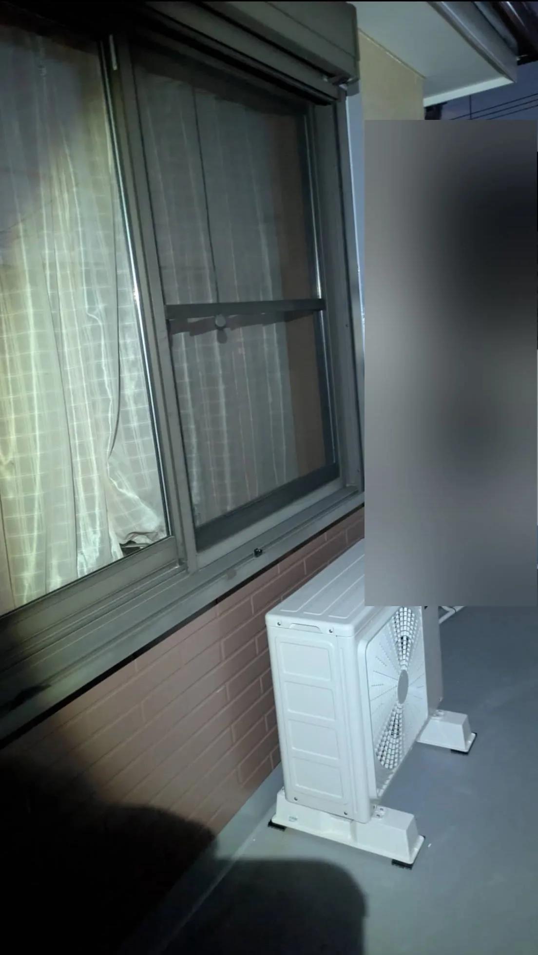 同じ部屋の室外機。ベランダの床に直接置かず、樹脂の台に載せて立ち上げ、配管は右の壁へ沿わせている