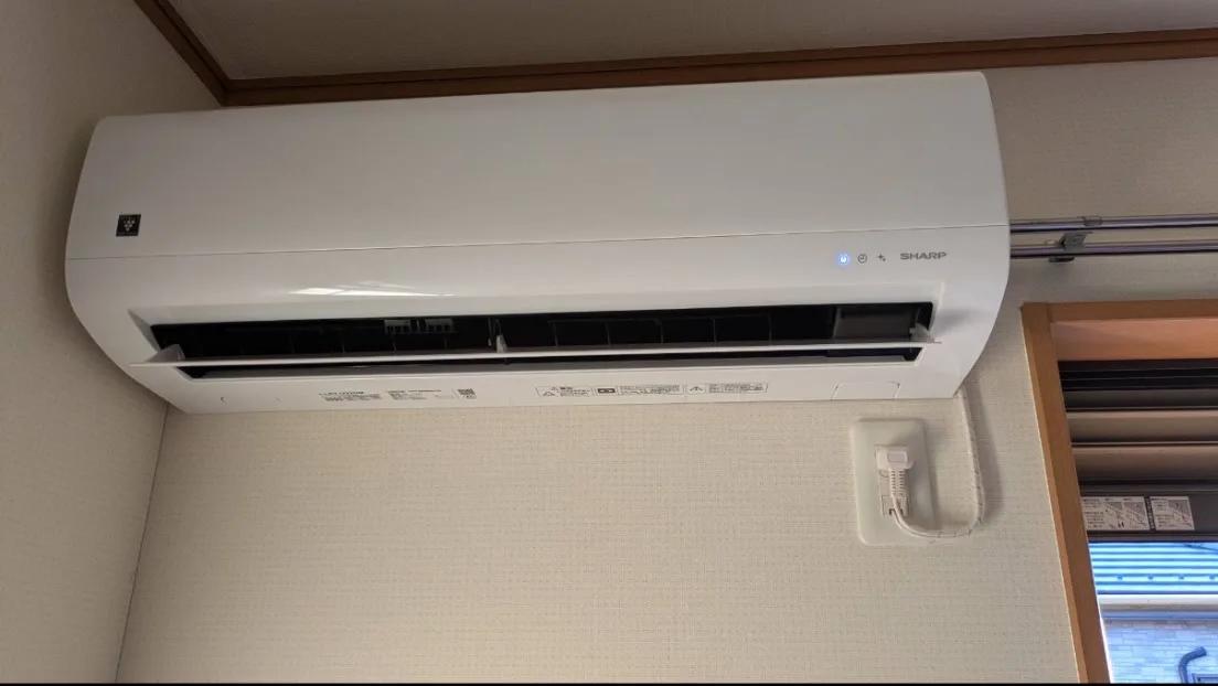 その部屋の室内機。窓の上の壁に取り付け、配管は右の窓側へ抜いている