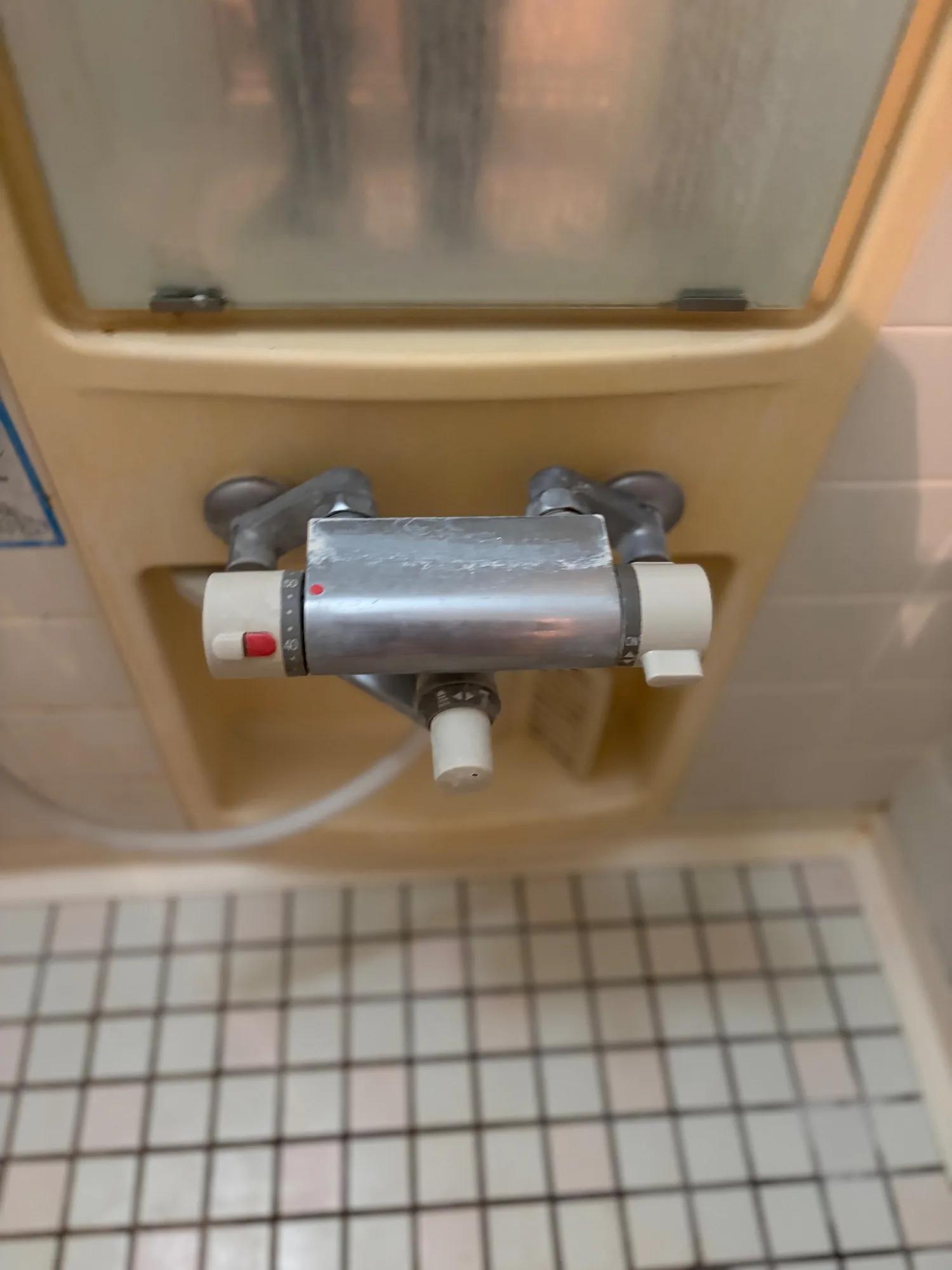 交換前の浴室水栓。壁のくぼみに付いたサーモスタット付き混合水栓で、本体の表面には白い水あかが固着している