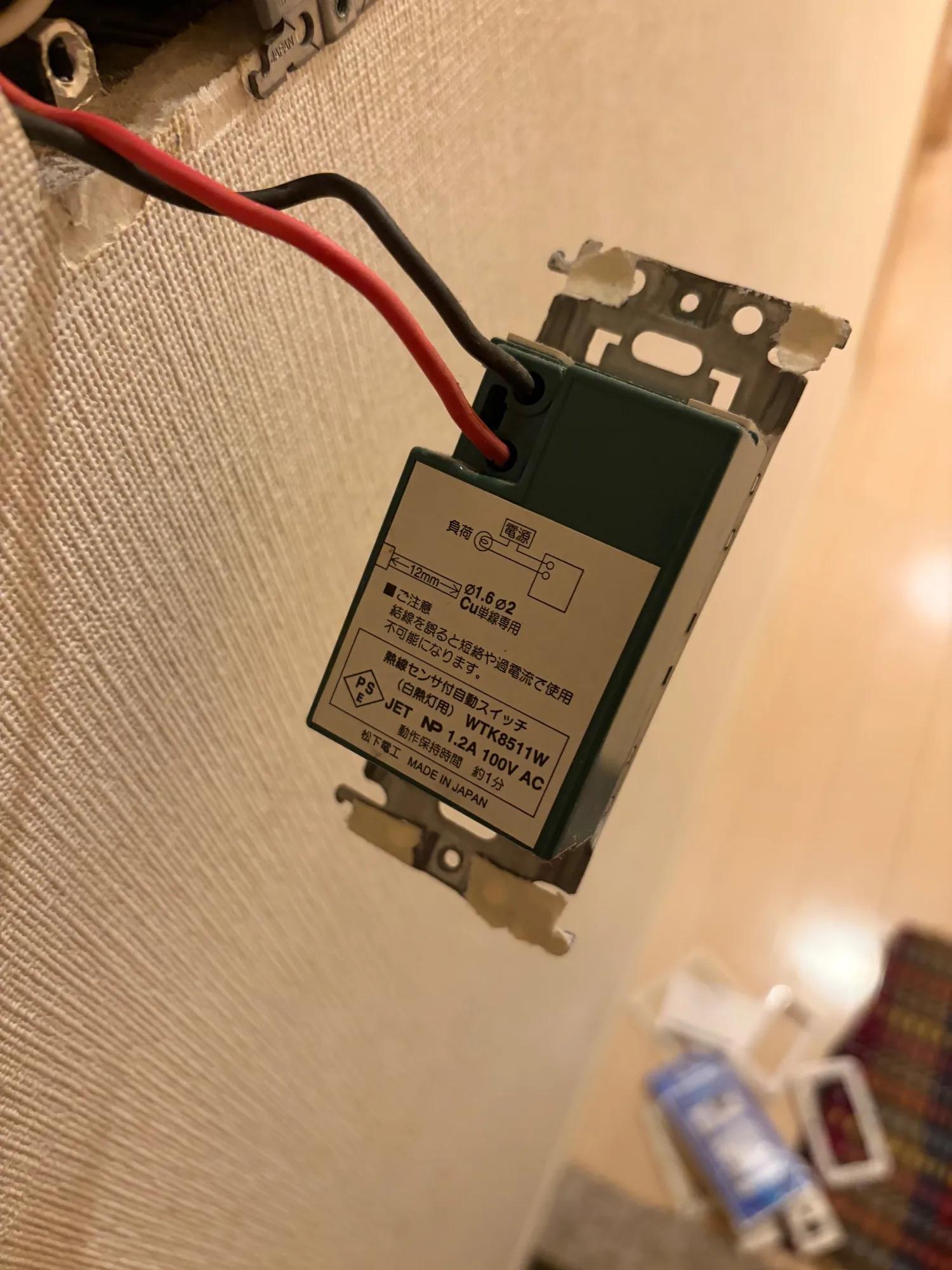 もともと付いていたスイッチ。品番 WTK8511W、熱線センサ付自動スイッチ（白熱灯用）。外す前に、赤と黒の線がどの端子に入っていたかを撮って残した